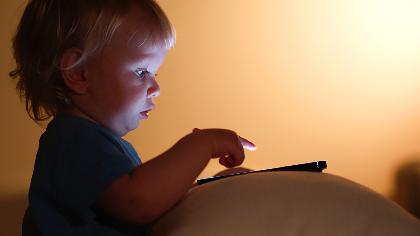 Criança pequena olhando tela de celular, para falar se o excesso de telas atrasa a fala