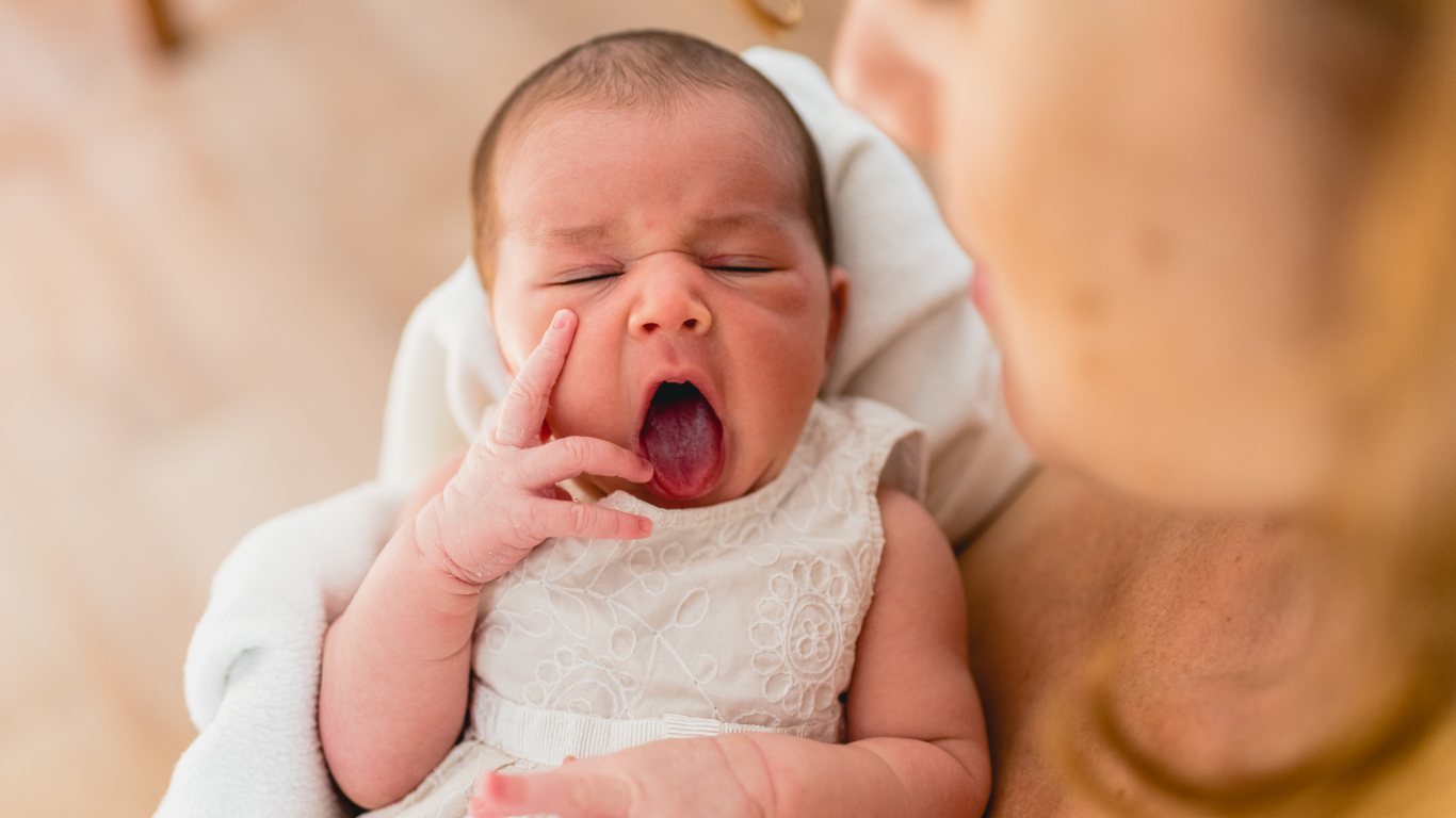 Recém nascida bocejando nos braços da mãe, para falar sobre o teste da linguinha e da orelhinha